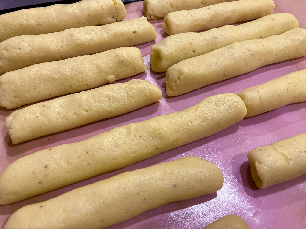 Rolls of gnocchi dough on a pink baking sheet