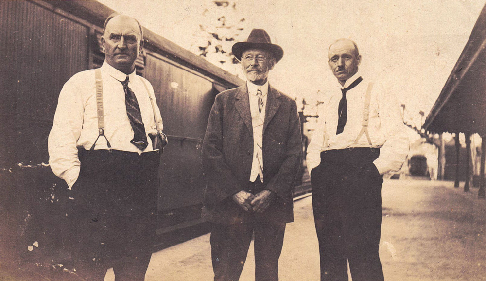 Three men in the early 20th century standing on a train platform in front of a train
