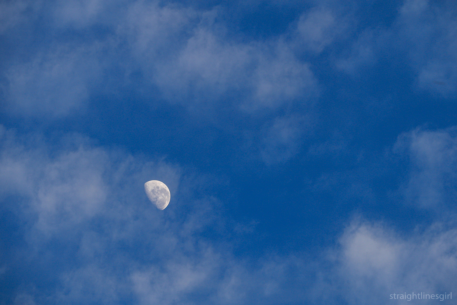A waning moon in a blue sky with white clouds