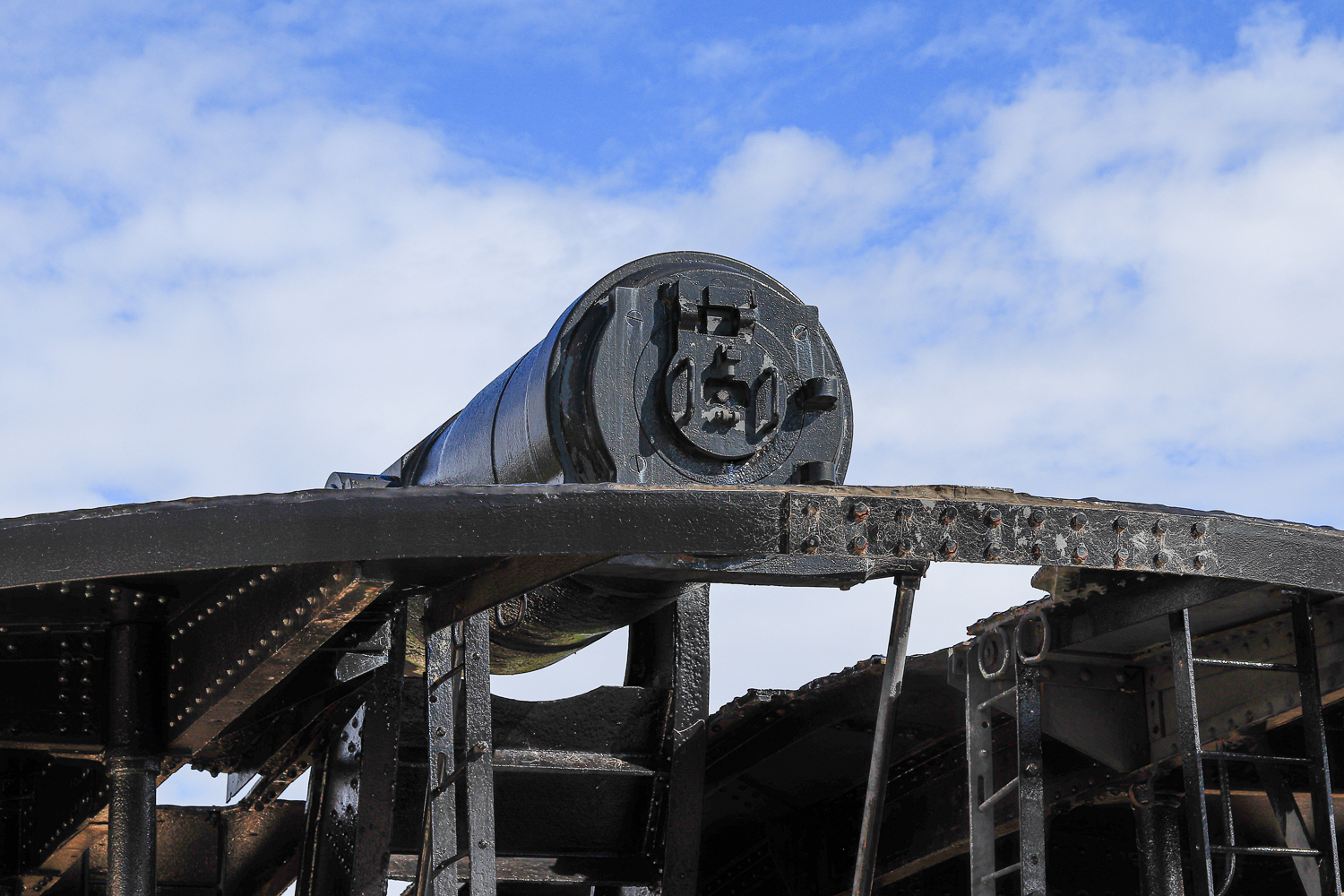 A close up of the back of a very large gun on a military base against blue sky
